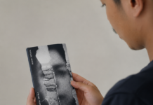 OPINI – Senjata Terakhir Menghadapi Genosida Gaza Seorang pria terlihat dari sisi belakang sedang membaca buku kecil bercover hitam putih bertuliskan Minor Detail karya Adania Shibli. Wajah pria hanya tampak sebagian dalam posisi profil.